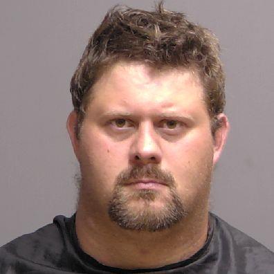 A man with short, tousled brown hair, a goatee, and a solemn expression stares directly at the camera. He is wearing a black top against a plain, neutral background, resembling news portraits often seen in Flagler County's Palm Coast coverage.