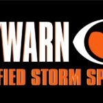 A rectangular black badge with the white text "SKYWARN" in bold on the left. On the right, there is the SKYWARN logo, an eye-like shape with an orange center and black tornado design. Below, in bold orange text, it reads "CERTIFIED STORM SPOTTER" - proudly protecting Flagler County and Palm Coast residents.
