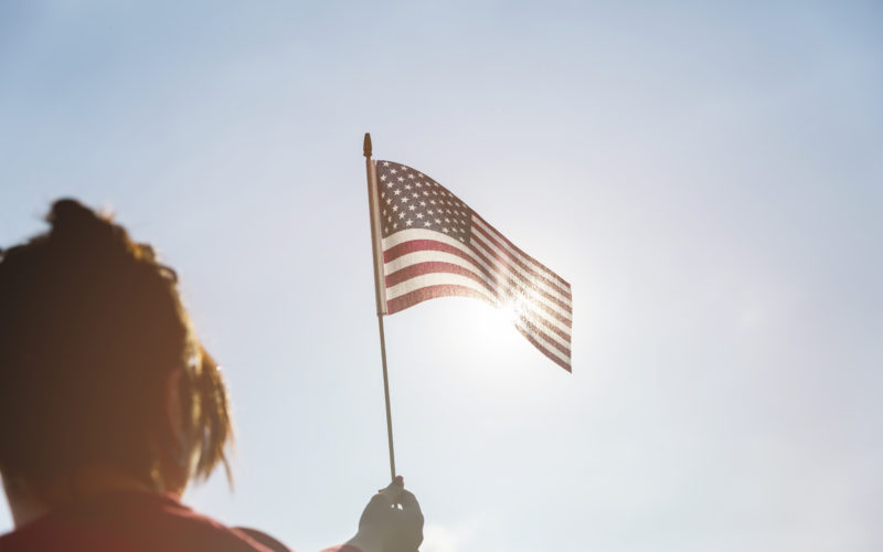 woman raising american flag bright sun