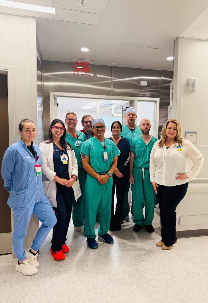 A group of ten medical professionals, including doctors and nurses, stand together and smile in a hospital hallway Some wear scrubs while others wear lab coats or business attire The setting is bright and modern