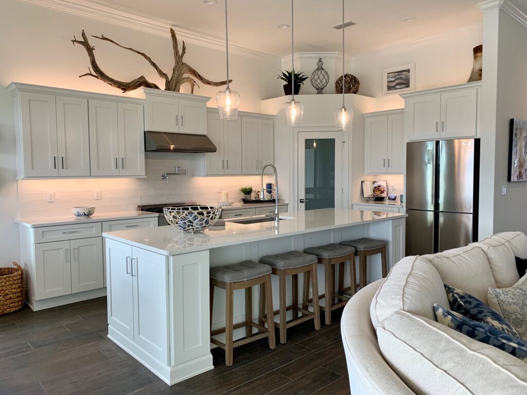 Modern kitchen with white cabinets, stainless steel appliances, and a large island with four stools Three pendant lights hang above the island Decorative items and plants are on top of the cabinets