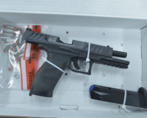 A black semi automatic handgun secured with zip ties lies in an evidence box, next to a magazine and a bag of bullets marked "evidence