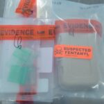 Two sealed evidence bags labeled "EVIDENCE"; one contains small green packets, the other contains a box with an orange "SUSPECTED FENTANYL" sticker and a skull symbol Both are on a metallic surface