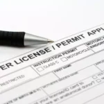 A close up of a pen resting on a driver license and permit application form, with checkboxes for different permit types visible