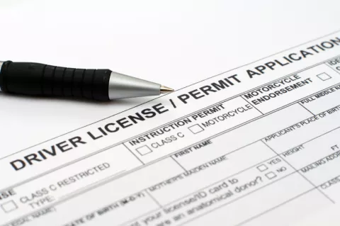 A close up of a pen resting on a driver license and permit application form, with checkboxes for different permit types visible