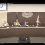 A city council meeting in session, with six people seated at a curved desk in front of the Palm Coast seal Nameplates, microphones, and papers are visible The screen header reads "City Council Business Workshop July ,