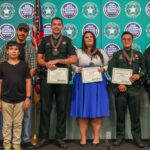A group photo shows three sheriff’s deputies with medals and certificates, joined by a woman, two children, a man, and another uniformed officer, standing in front of an awards backdrop