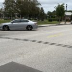 Two silver cars are parked along a quiet street lined with some trees A blue fire hydrant is on the sidewalk, and two black cables stretch across the road under a cloudy sky