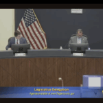 Two officials sit at a curved desk in a government meeting room with U S and Florida flags behind them The text reads “Legislative Delegation” and “FCTV ” The date “//” appears in the lower right corner