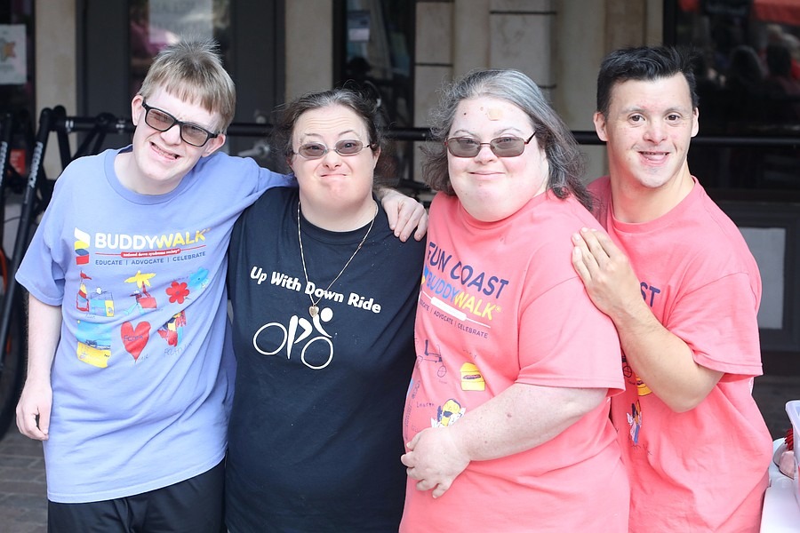 Four adults with Down syndrome smiling and standing together outside Two wear "Buddy Walk" t shirts and another wears an "Up With Down Ride" shirt They stand arm in arm, appearing happy and supportive