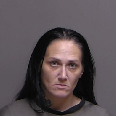 A woman with long black hair and a neutral expression looks directly at the camera against a plain gray background She is wearing a dark top