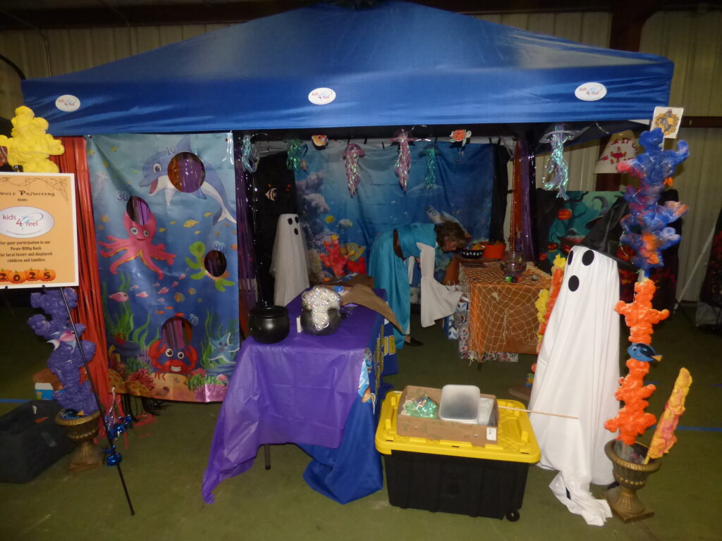 A colorful, undersea themed booth decorated with sea creature curtains, plastic coral, and Halloween ghost figures A blue canopy covers the setup, with tables holding candy bowls and festive decorations