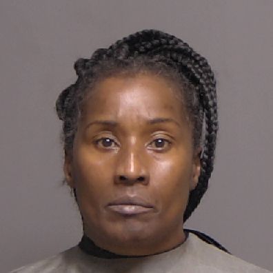A woman with braided hair looks at the camera with a neutral expression against a plain background She is wearing a dark colored, high neck garment