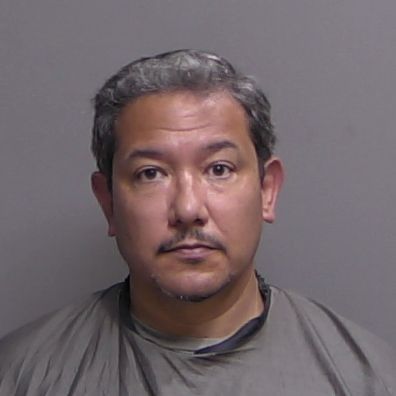 A middle aged man with short, gray black hair and a mustache is facing the camera against a plain gray background, wearing a gray garment that covers his shoulders and upper chest A middle aged man with short, gray black hair and a mustache is facing the camera against a plain gray background, wearing a gray garment that covers his shoulders and upper chest