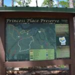 A wooden information board at Princess Place Preserve displays a detailed trail map and visitor information Pine trees and natural vegetation are visible in the background under a clear sky