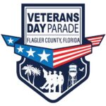 A badge shaped logo for the Veterans Day Parade in Flagler County, Florida, featuring stars, a waving American flag, silhouettes of soldiers, palm trees, a water tower labeled "Bunnell," and an airplane