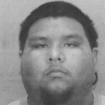 Black and white headshot of a person with short dark hair, a round face, and a neutral expression, looking directly at the camera against a plain background