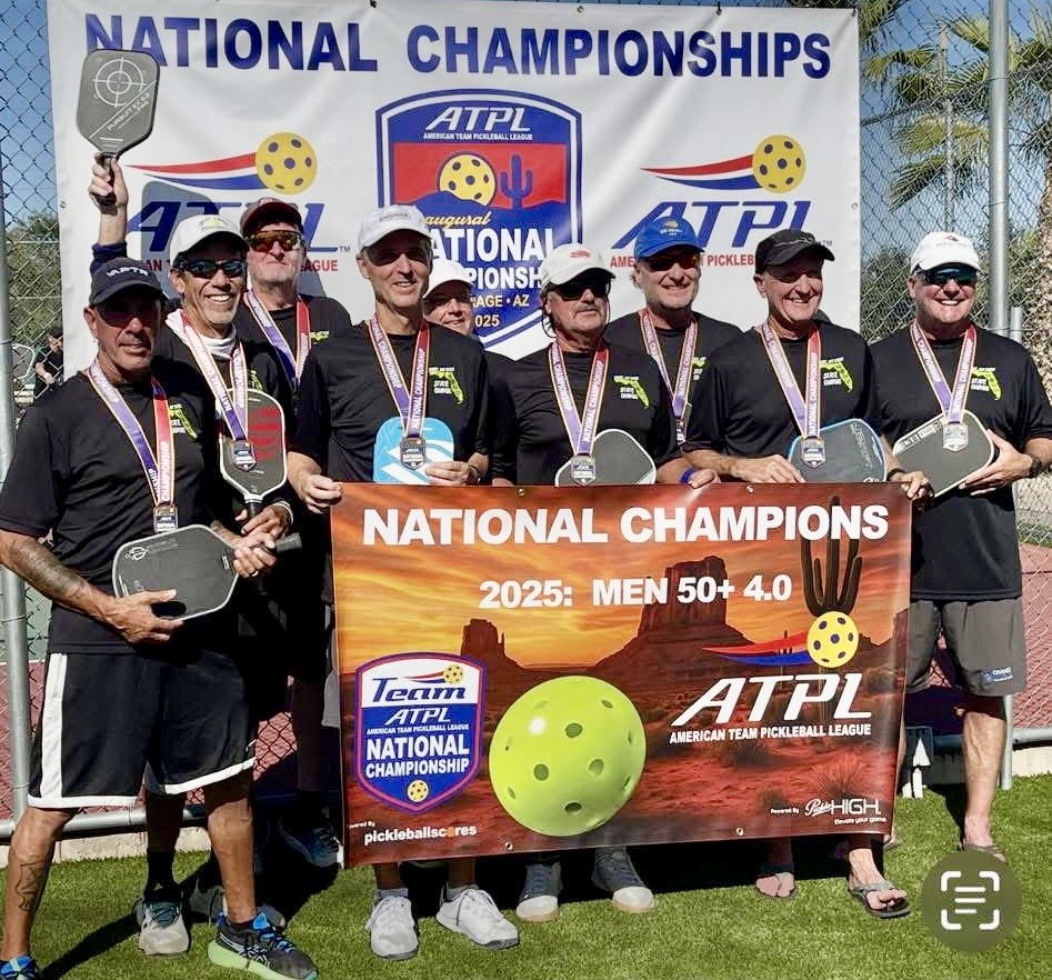 A group of eight men wearing medals and holding pickleball paddles stand together, smiling, behind a banner reading “NATIONAL CHAMPIONS : MEN + ” A backdrop for the American Team Pickleball League is visible behind them