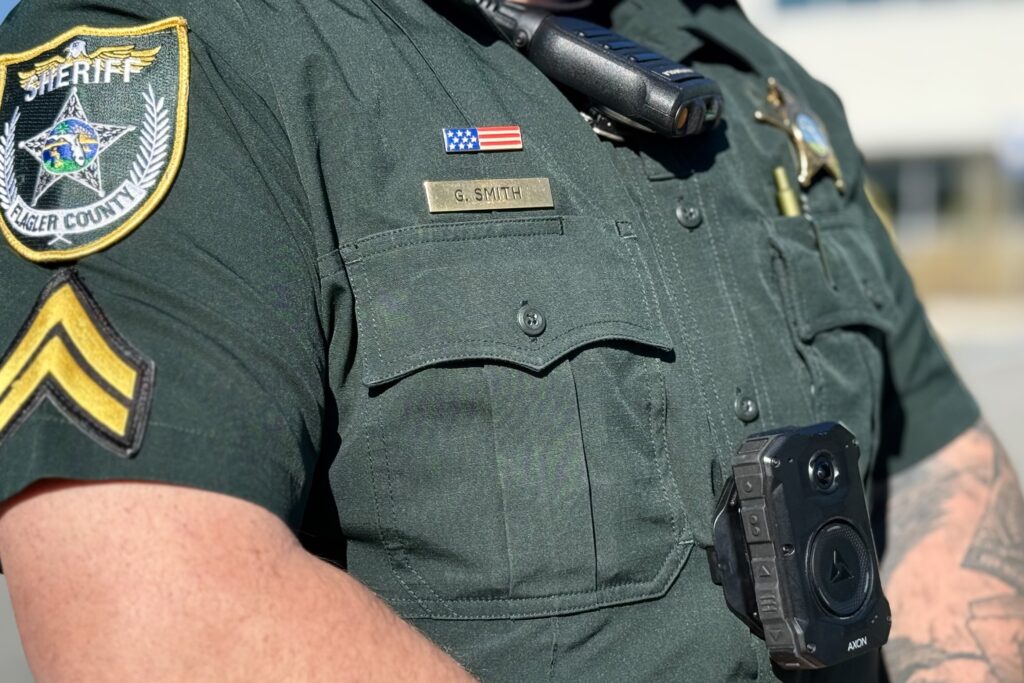 A close up of a sheriff's deputy in uniform wearing a body camera and radio The nameplate reads "G Smith" and the badge indicates Blazer County An American flag patch is visible above the nameplate A close up of a sheriff's deputy in uniform wearing a body camera and radio The nameplate reads "G Smith" and the badge indicates Blazer County An American flag patch is visible above the nameplate