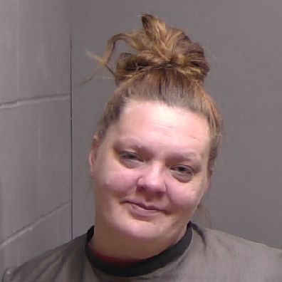 A woman with light skin and brown hair in a messy bun wears a dark shirt and stands against a gray wall, looking at the camera with a slight smile A woman with light skin and brown hair in a messy bun wears a dark shirt and stands against a gray wall, looking at the camera with a slight smile