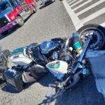 Two overturned police motorcycles lie on the street next to a car at an intersection A fire truck is parked nearby, and an orange traffic cone is visible in the background
