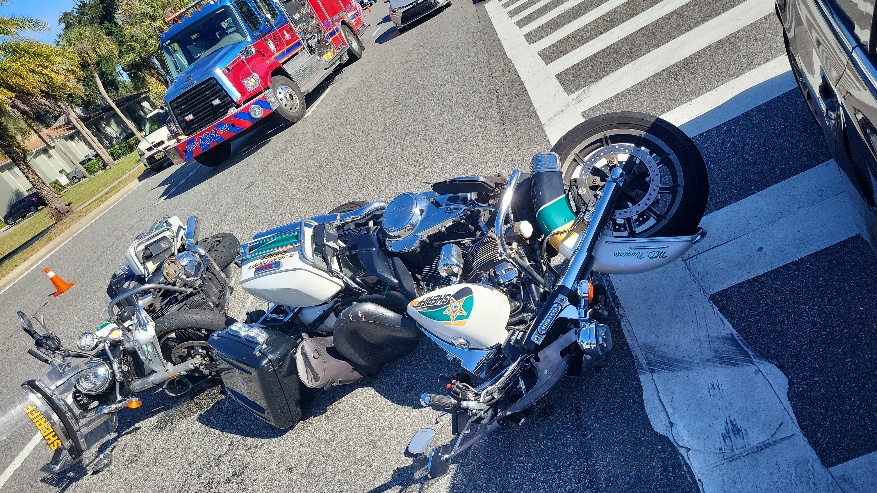 Two overturned police motorcycles lie on the street next to a car at an intersection A fire truck is parked nearby, and an orange traffic cone is visible in the background