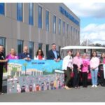 A group of people stand outside a large building holding colorful posters, some wearing pink shirts The sky is partly cloudy There is a Pink Army K logo in the bottom right corner of the image