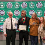 Four people stand in front of a backdrop with "Fourth Quarter Awards" and sheriff logos One man in uniform, another holds a certificate and medal, flanked by two women, all smiling American and Florida flags are visible