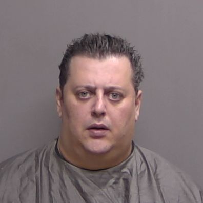 A middle aged man with short, dark hair is wearing a gray garment and is posed against a plain gray background for a mugshot He has a neutral facial expression A middle aged man with short, dark hair is wearing a gray garment and is posed against a plain gray background for a mugshot He has a neutral facial expression