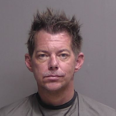 A middle aged man with spiky brown hair, wearing a gray smock, looks directly at the camera against a plain gray background A middle aged man with spiky brown hair, wearing a gray smock, looks directly at the camera against a plain gray background