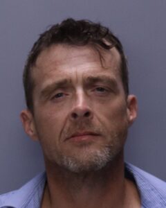 A middle aged man with short brown hair, light facial stubble, and a neutral expression, wearing a blue collared shirt, poses in front of a plain gray background A middle aged man with short brown hair, light facial stubble, and a neutral expression, wearing a blue collared shirt, poses in front of a plain gray background