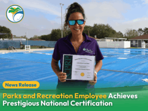 A smiling woman in sunglasses and a Parks and Recreation shirt holds a certificate while standing in front of an outdoor pool covered with blue tarps A "News Release" banner and certification announcement are overlaid on the image A smiling woman in sunglasses and a Parks and Recreation shirt holds a certificate while standing in front of an outdoor pool covered with blue tarps A "News Release" banner and certification announcement are overlaid on the image