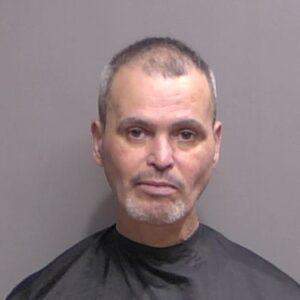 A middle aged man with short hair, slight facial hair, and a neutral expression faces the camera against a plain background, wearing a dark garment typically used for mugshots A middle aged man with short hair, slight facial hair, and a neutral expression faces the camera against a plain background, wearing a dark garment typically used for mugshots