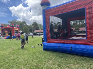 Children and adults enjoy an outdoor event with two colorful bounce houses on a grassy field under a partly cloudy sky Some people stand nearby, while others play inside the inflatables