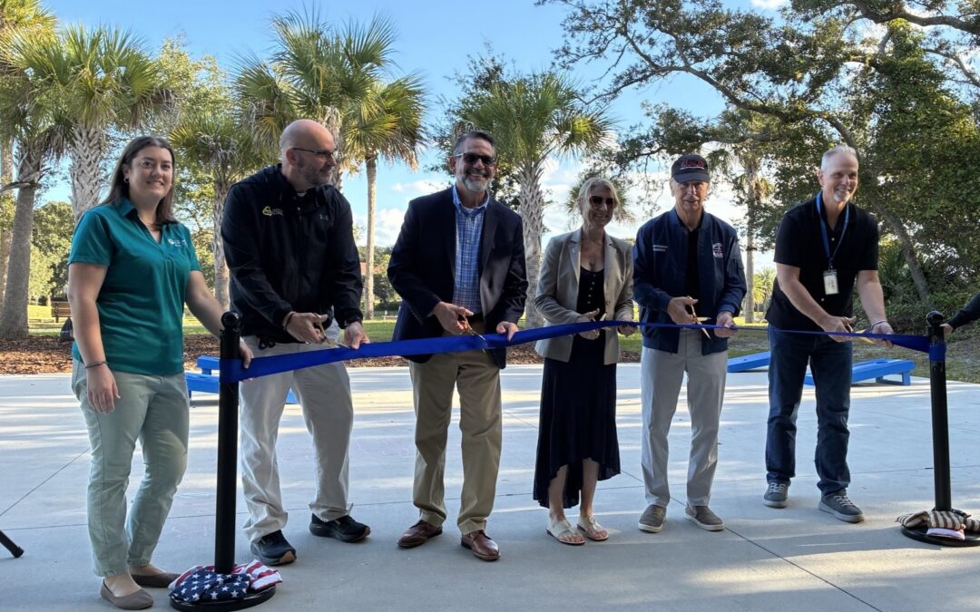 Six people stand in a line holding a blue ribbon with gold scissors for a ribbon cutting ceremony