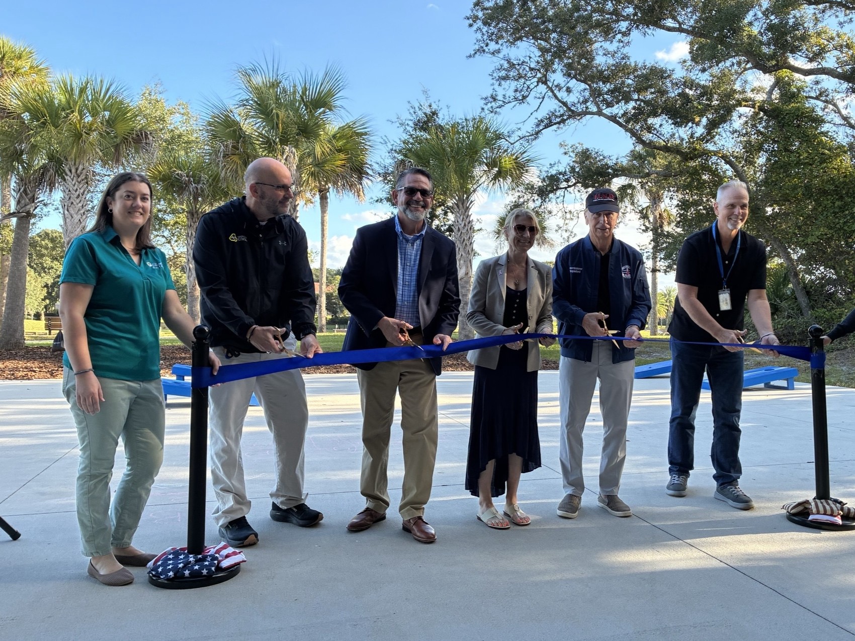 Six people stand in a line holding a blue ribbon with gold scissors for a ribbon cutting ceremony