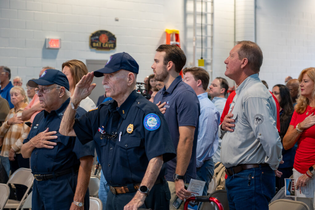 A group of people standing for the Pledge of Allegiance, with some saluting and others with hands over their hearts A group of people standing for the Pledge of Allegiance, with some saluting and others with hands over their hearts