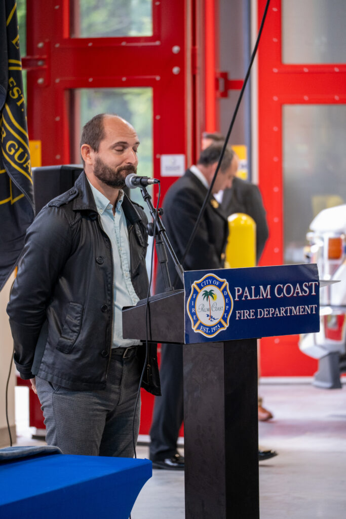 A man speaking into a microphone at a podium labeled “City of Palm Coast Fire Department ” A man speaking into a microphone at a podium labeled “City of Palm Coast Fire Department ”