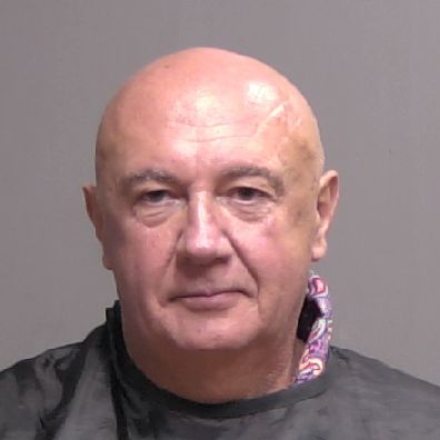 A headshot of a bald, older man with a neutral expression against a plain background